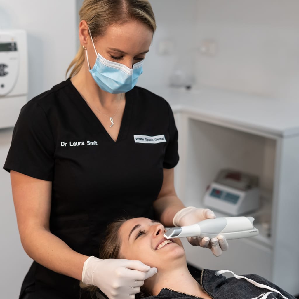 Dr. Laura Smit uses an intraoral scanner on a smiling patient during a consultation to get her teeth whitened at the dentist.